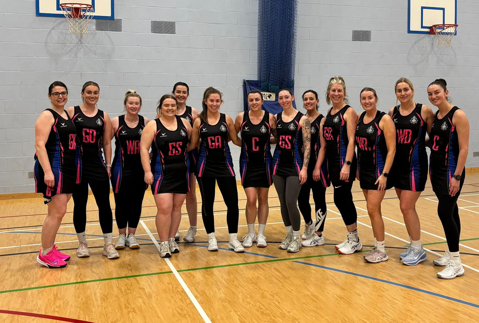 Durham Police Netball Team in their black and pink match kit, lined up on court