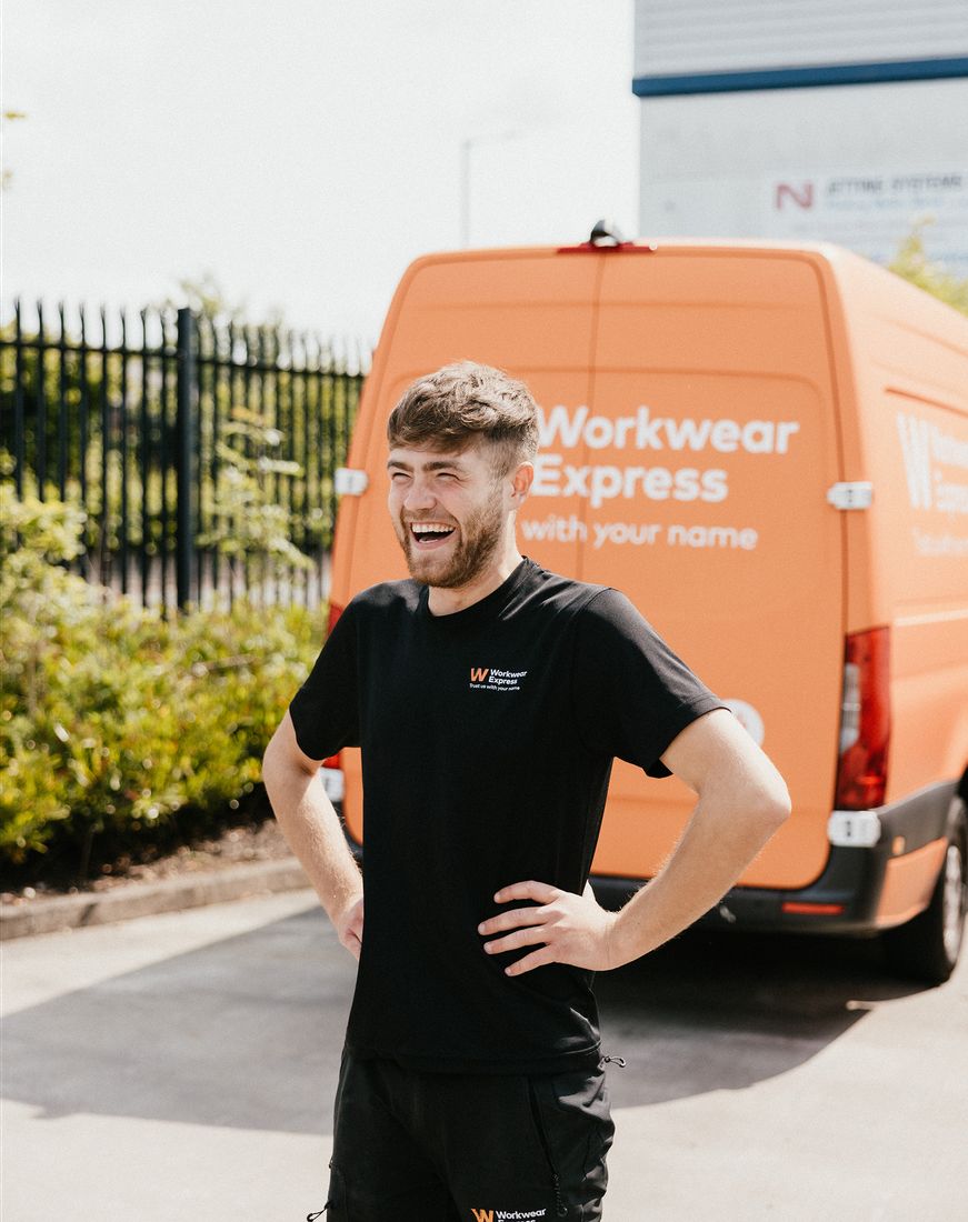 A Workwear Express team member laughing in front of an orange Workwear Express delivery van